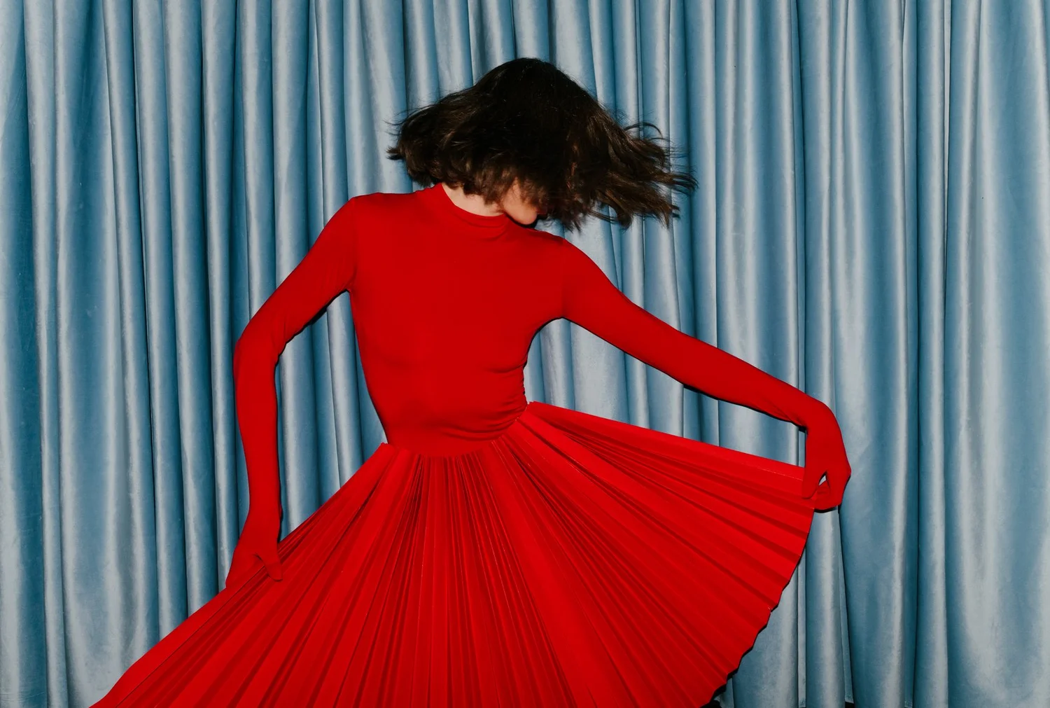 Model in a red pleated gown against a blue velvet curtain